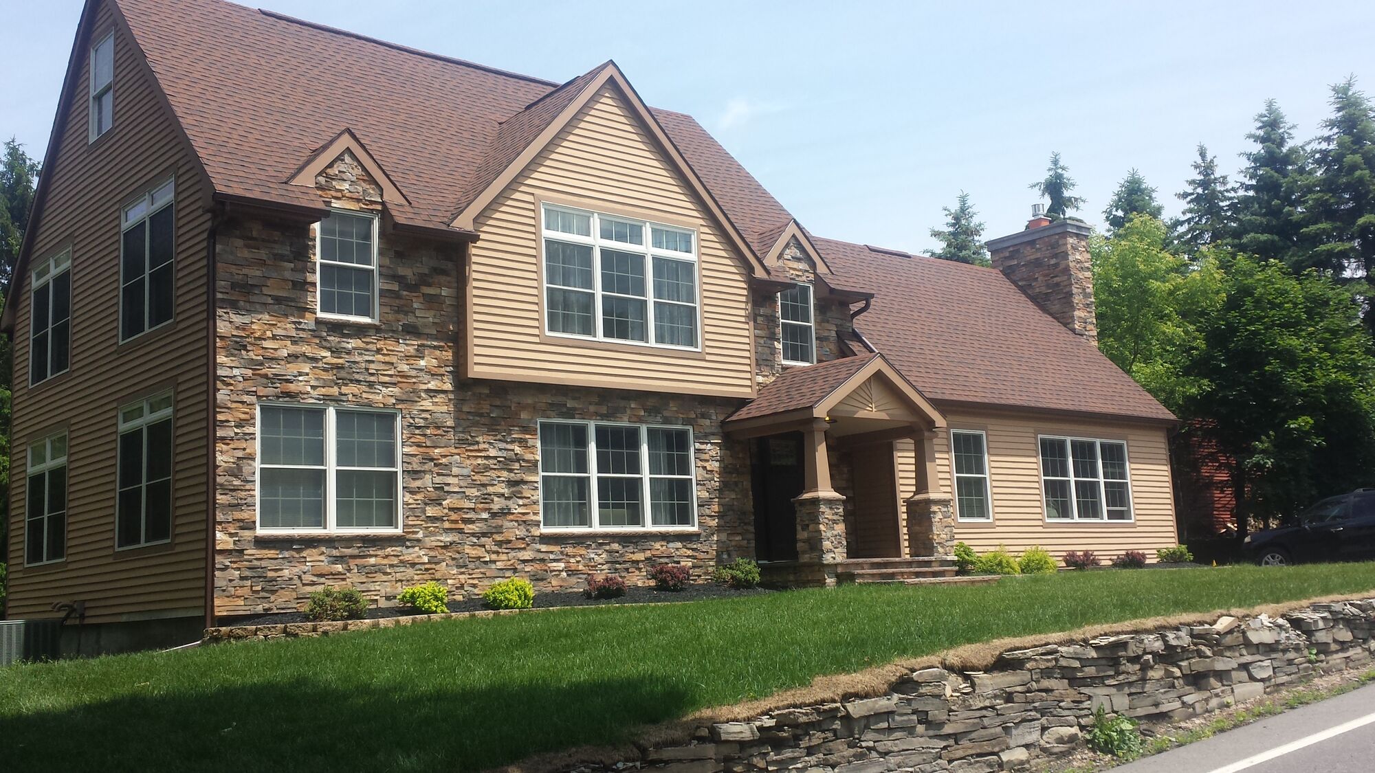 Custom stone-veneer home with a natural stacked-stone retaining wall and stone chimney, built by CNY Chimney & Masonry