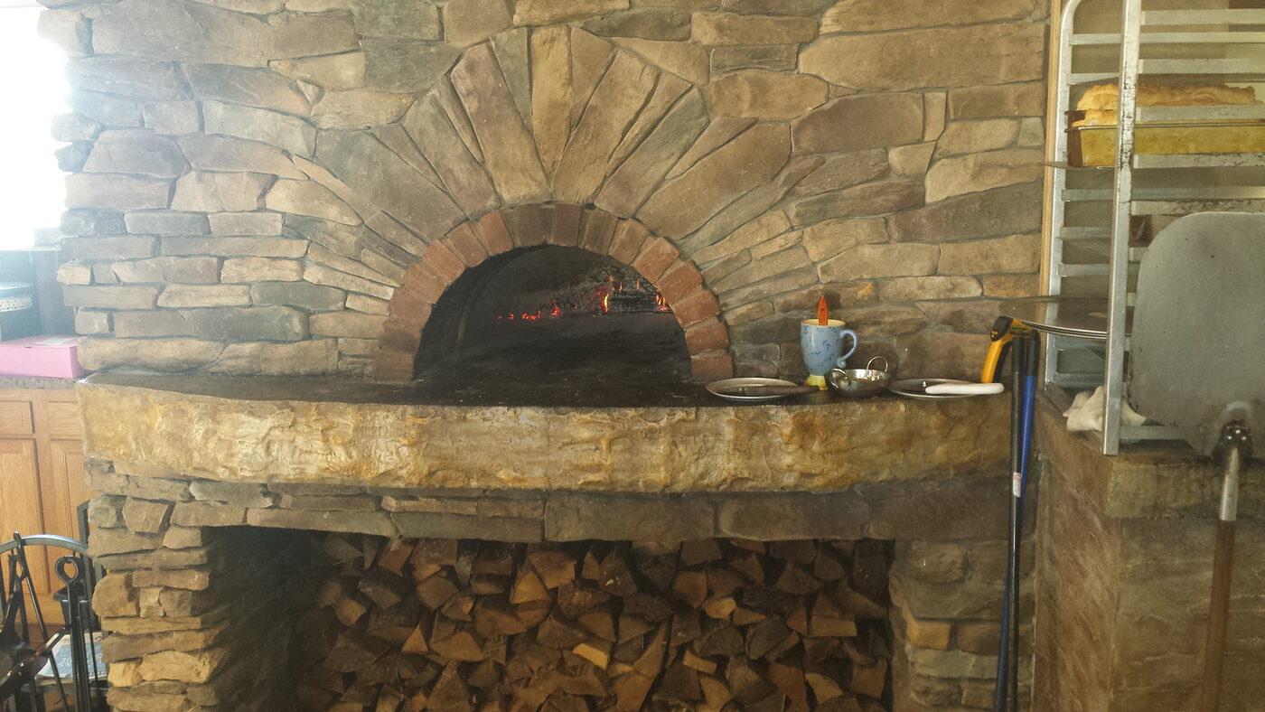 Custom outdoor wood-fired brick pizza oven with a stone arch and lit fire
