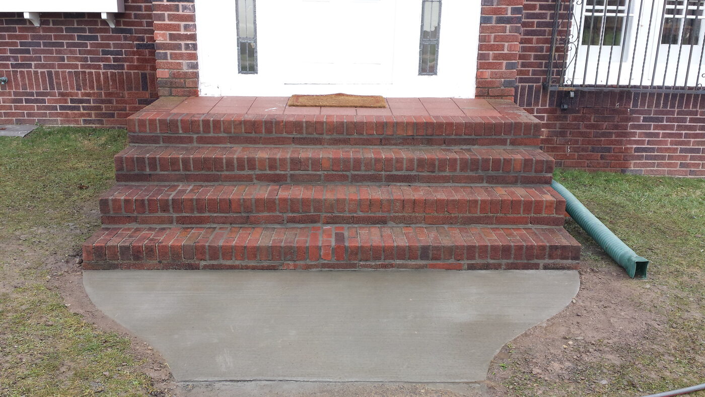 Red brick steps with railings and a new concrete walkway