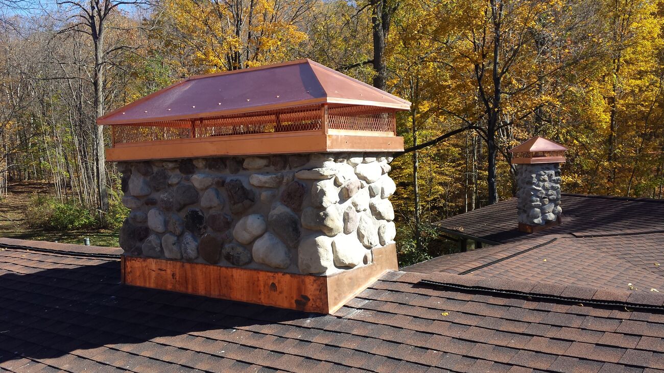 Stone-veneer chimney topped with a custom copper chase cover in an autumn setting